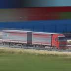 Camion in corsa sulla tangenziale con i magazzini dell'Interporto sullo sfondo dipinti a riquadri molto vivaci